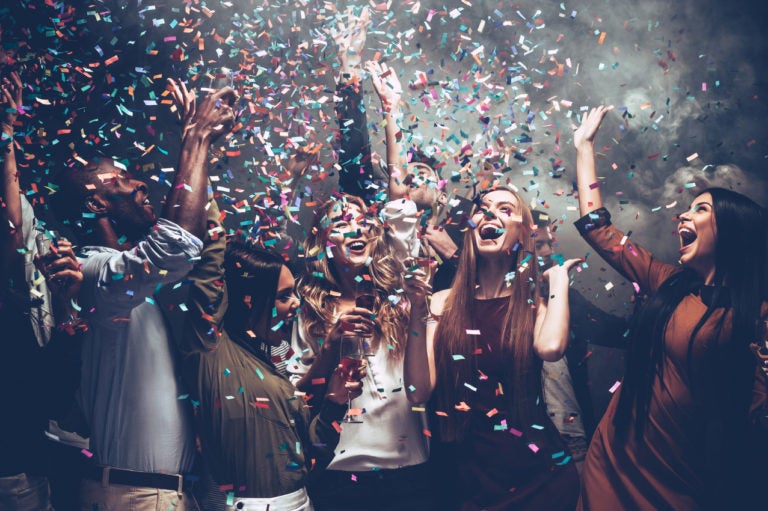 Group of beautiful young people throwing colorful confetti while dancing and looking happy